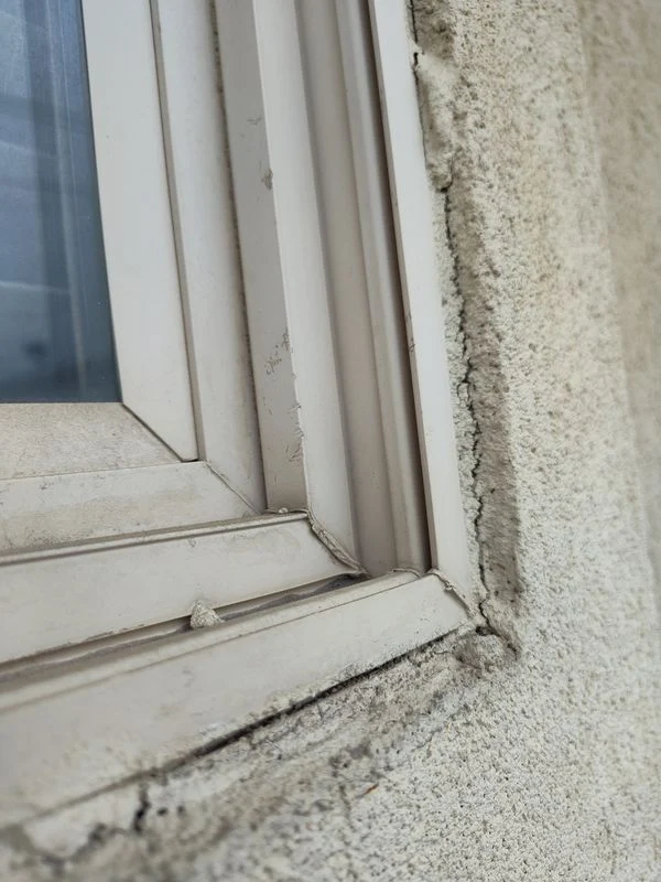 Cracking and dark staining along the joint beside a window