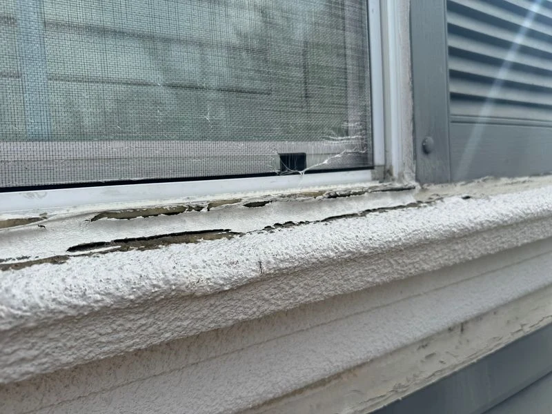 Close-up of cracking and a deteriorated joint beneath a stucco window